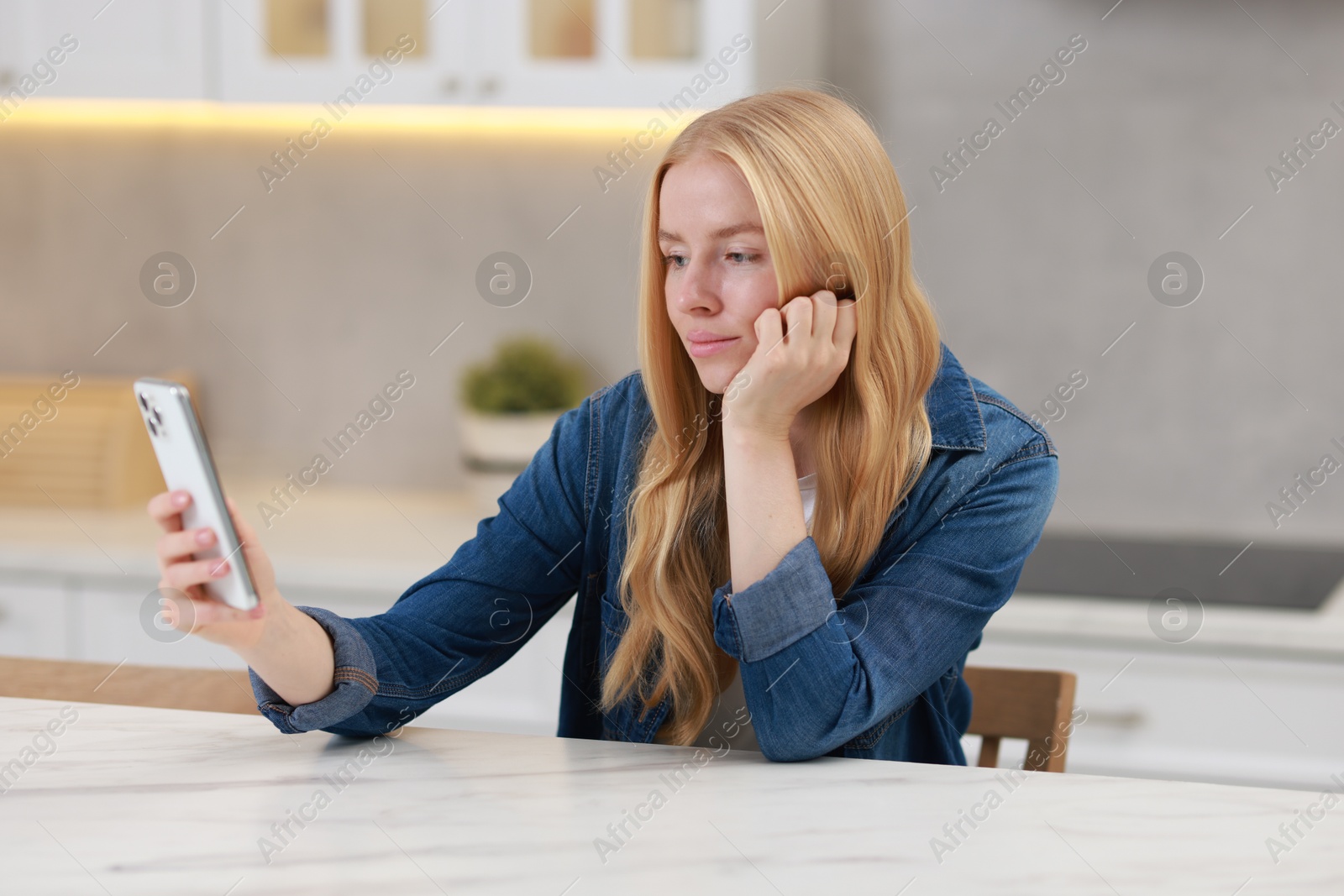 Photo of Beautiful woman using smartphone at white table in kitchen