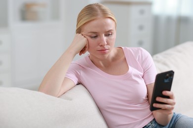 Beautiful woman using smartphone on sofa indoors