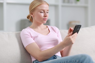 Beautiful woman using smartphone on sofa indoors