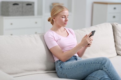 Photo of Beautiful woman using smartphone on sofa indoors