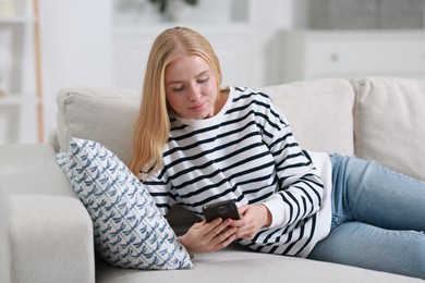 Beautiful woman using smartphone on sofa indoors