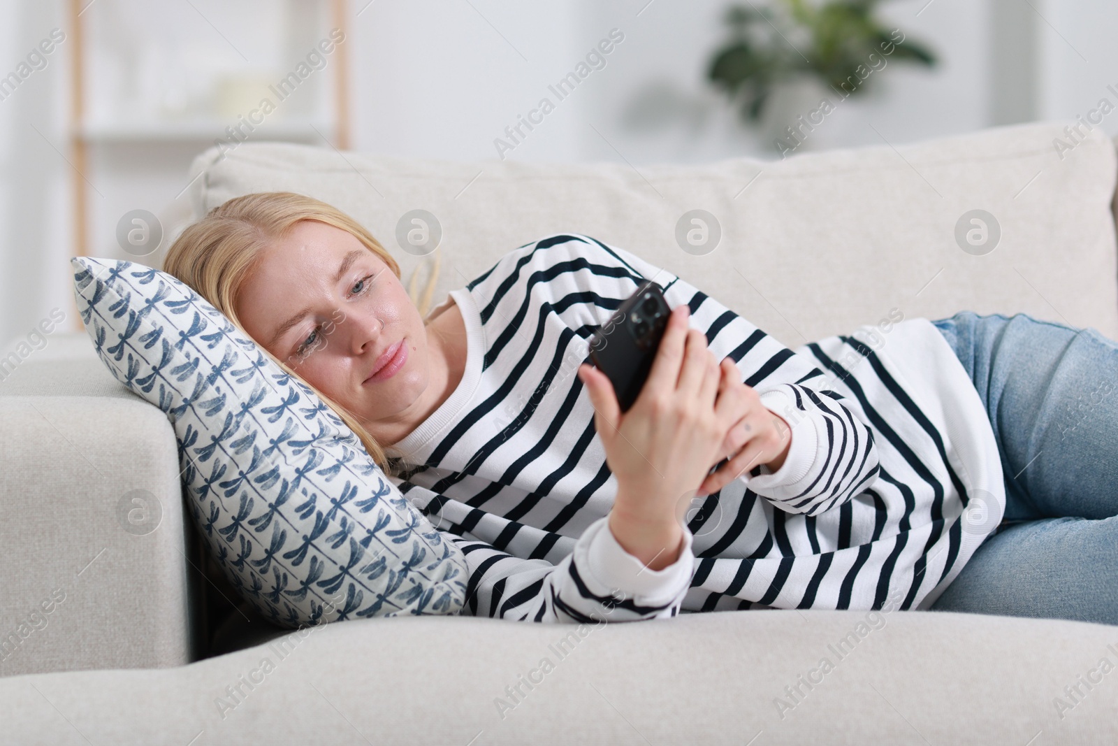 Photo of Beautiful woman using smartphone on sofa indoors