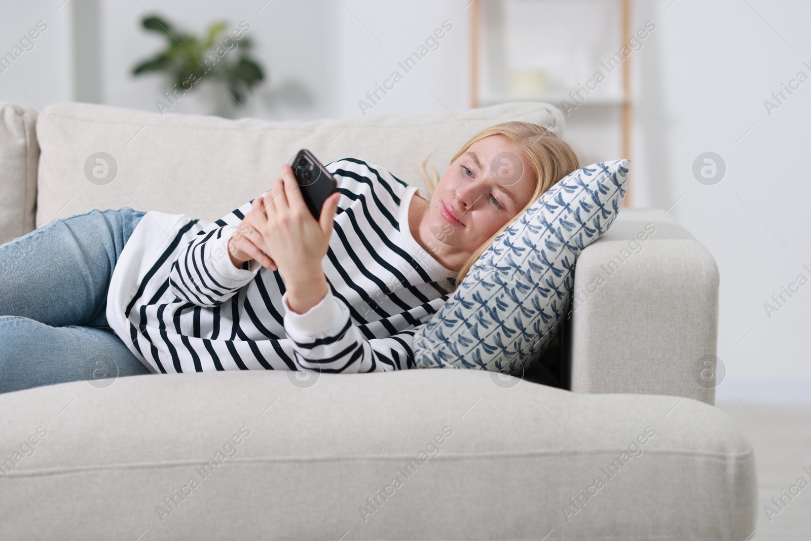 Photo of Beautiful woman using smartphone on sofa indoors