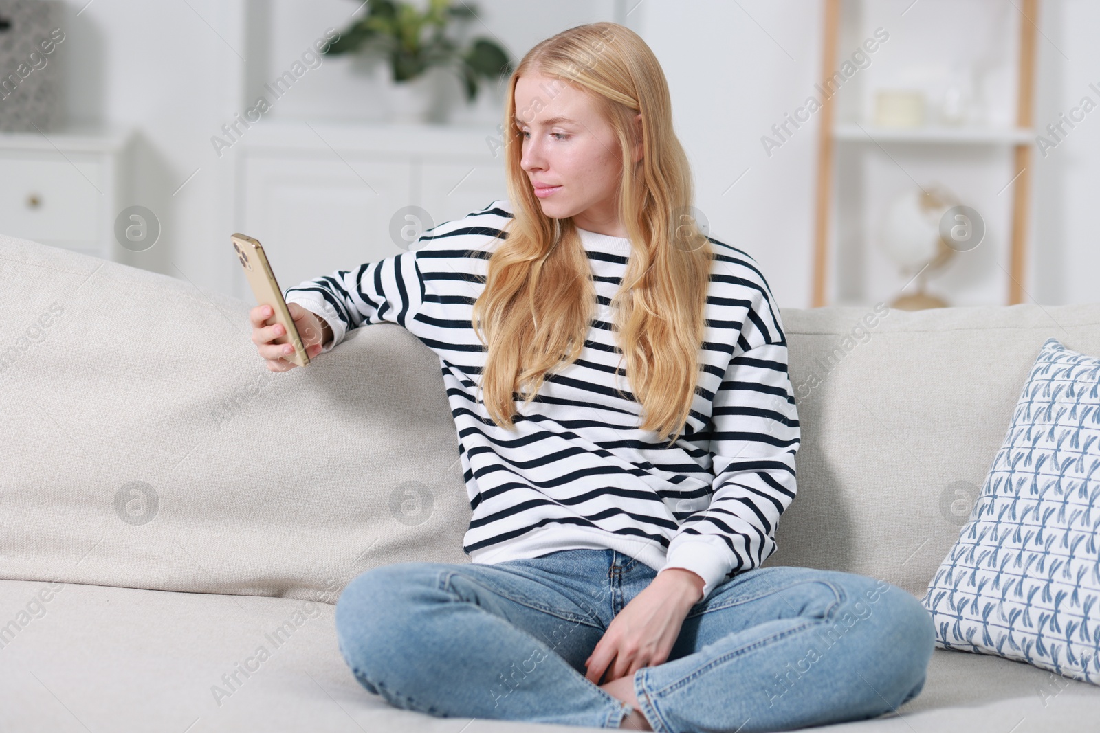 Photo of Beautiful woman using smartphone on sofa indoors