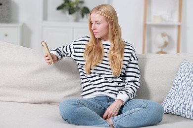 Photo of Beautiful woman using smartphone on sofa indoors