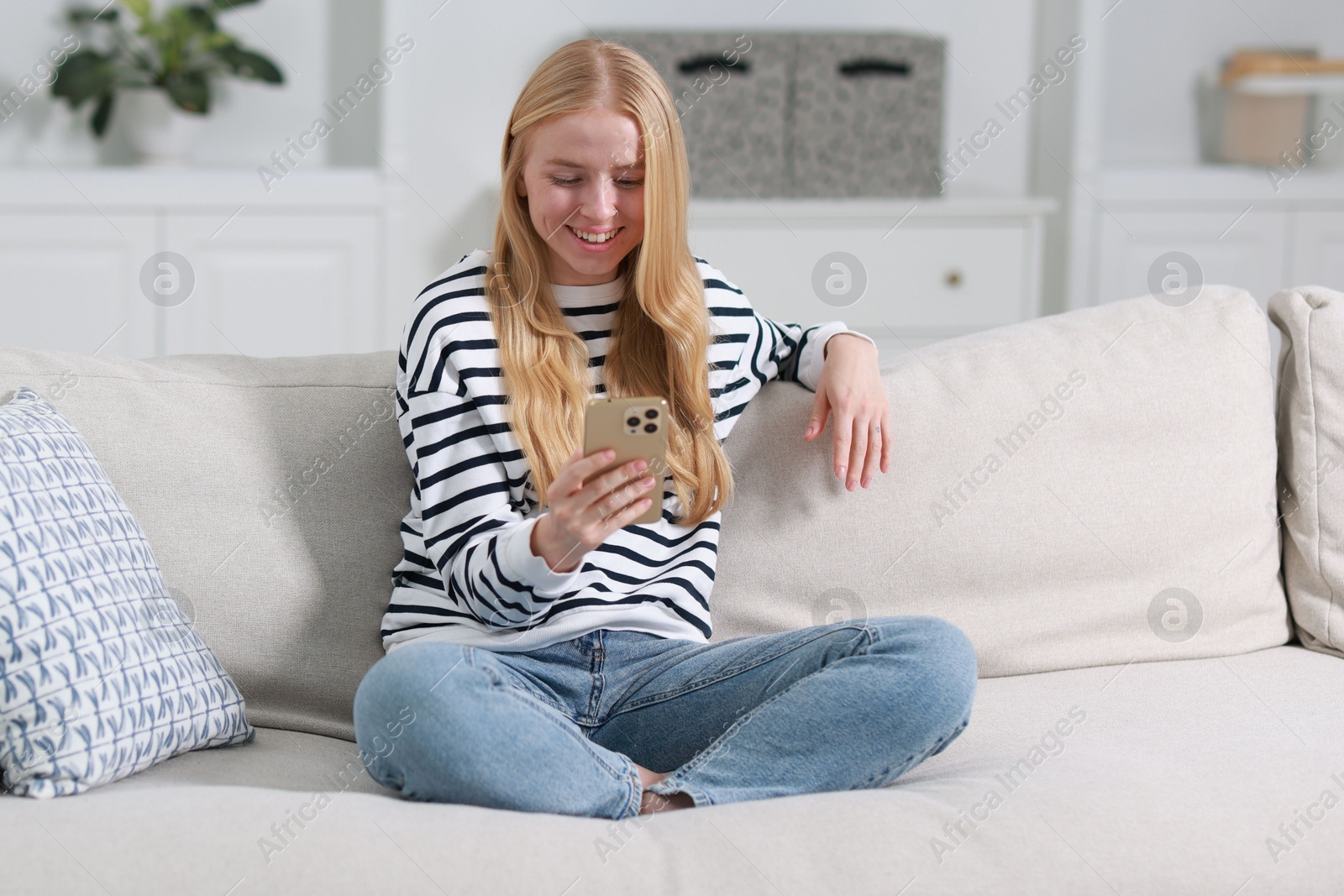 Photo of Smiling woman using smartphone on sofa indoors