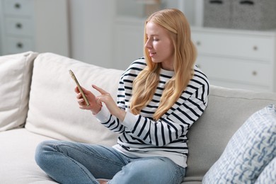 Photo of Beautiful woman using smartphone on sofa indoors