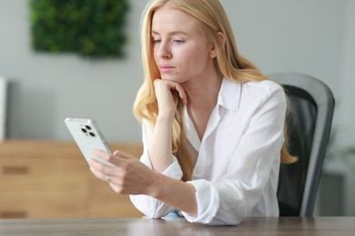 Beautiful woman using smartphone at table in office