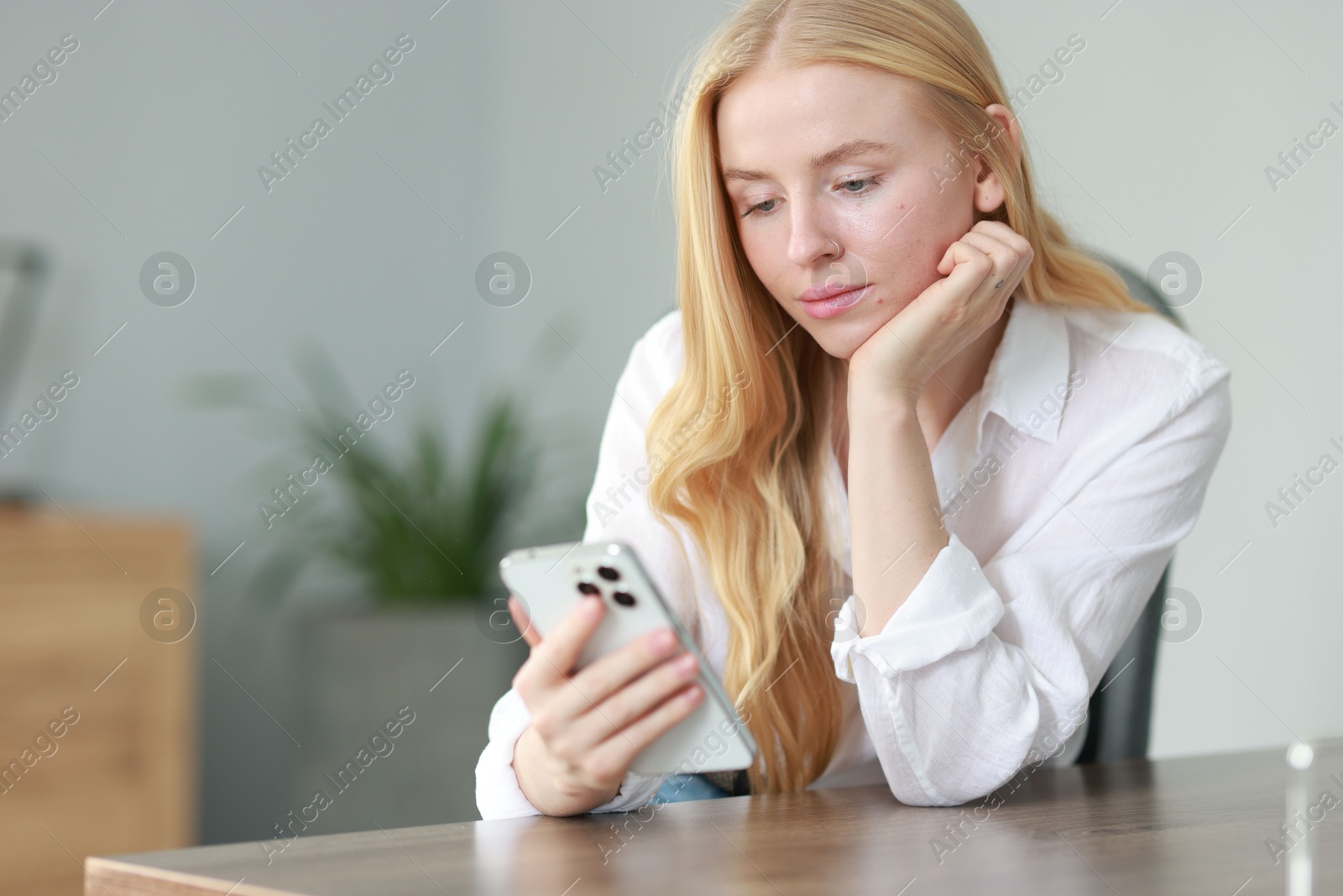 Photo of Beautiful woman using smartphone at table in office. Space for text