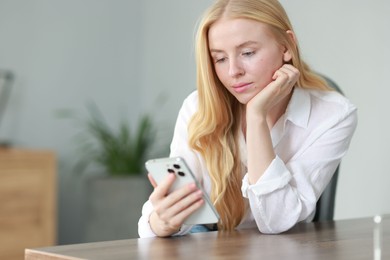 Beautiful woman using smartphone at table in office. Space for text