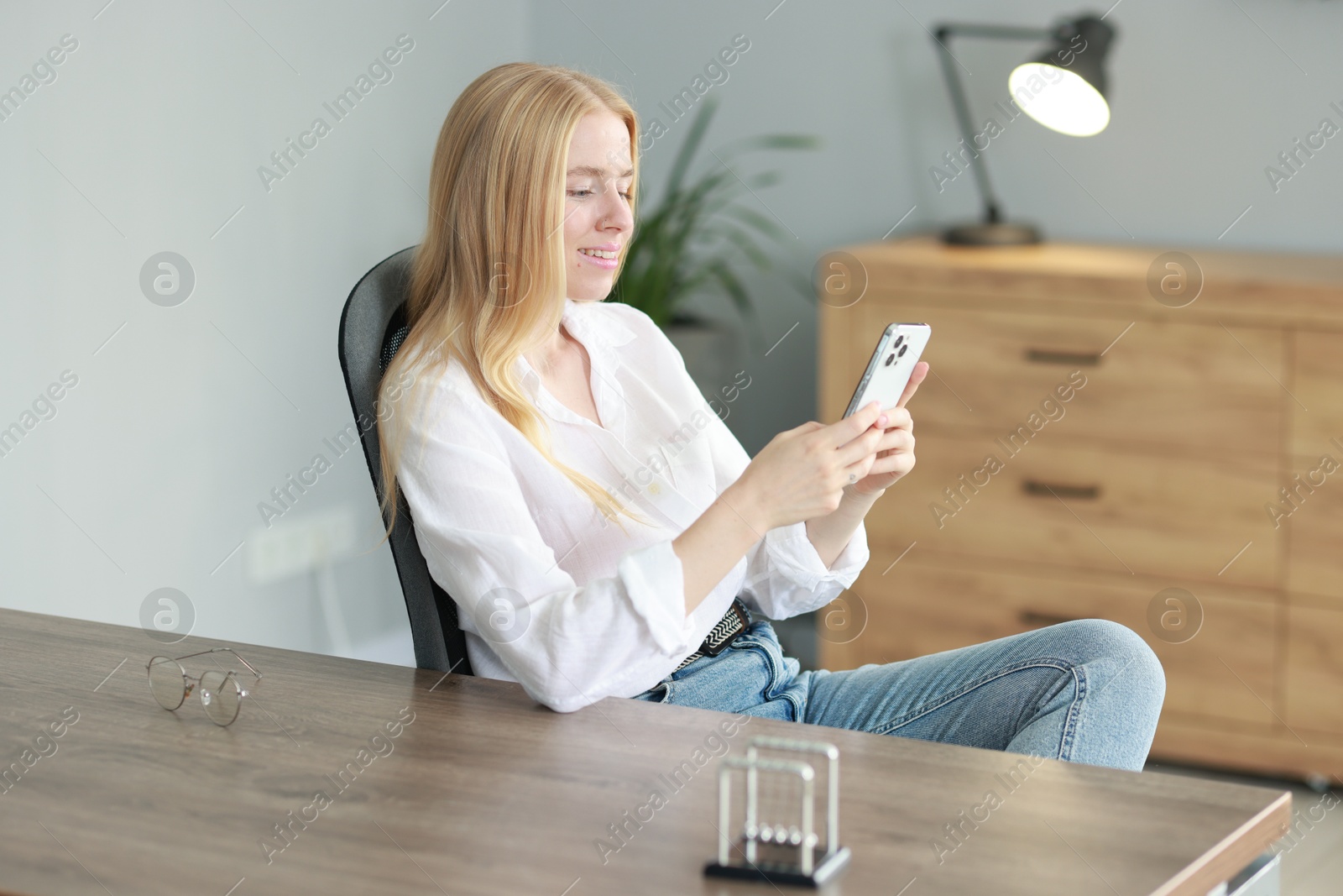 Photo of Smiling woman using smartphone at table in office