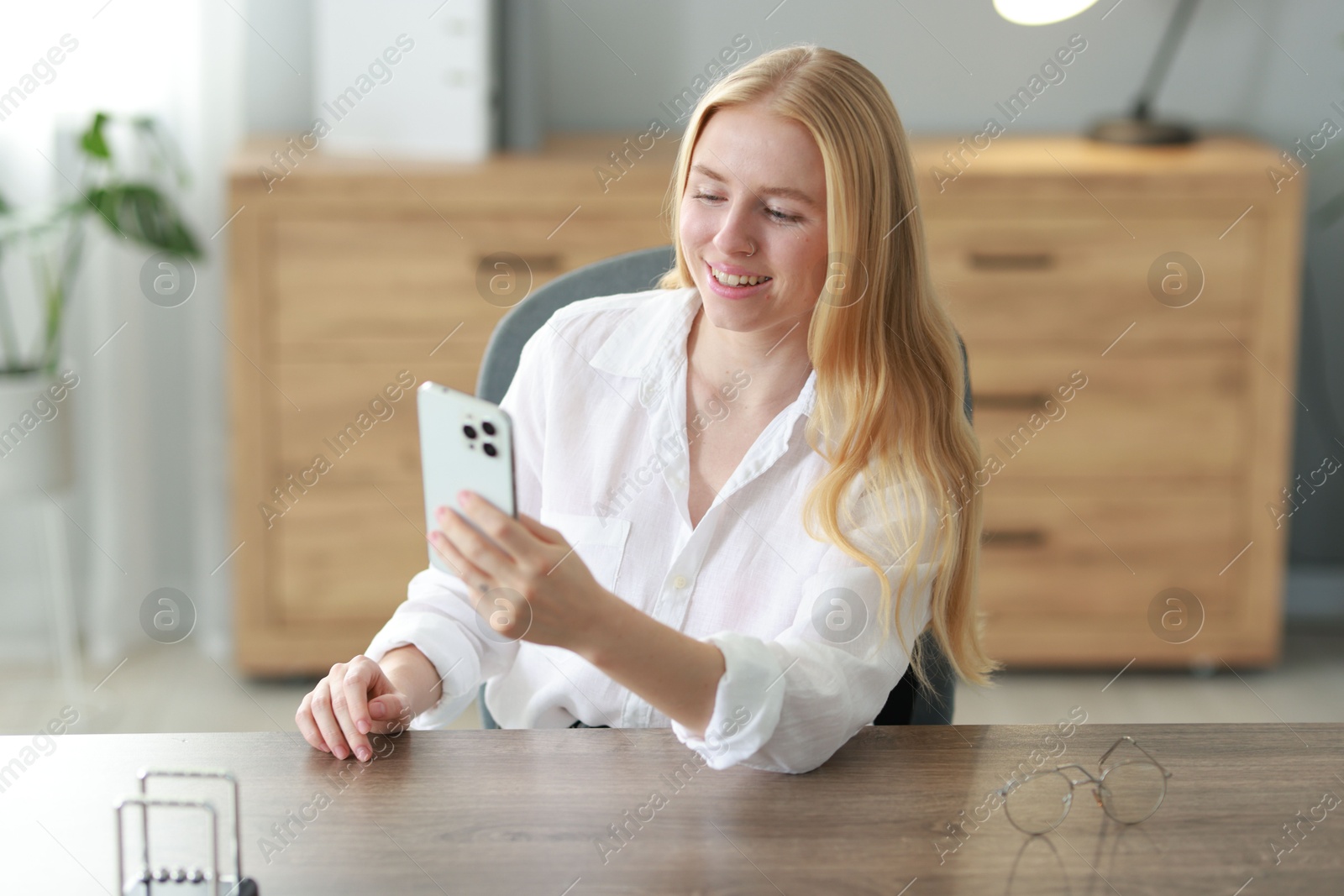 Photo of Smiling woman using smartphone at table in office