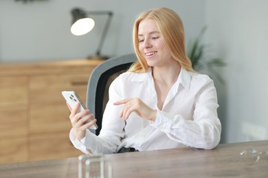 Smiling woman using smartphone at table in office