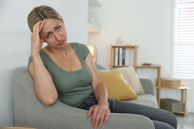 Photo of Menopause. Woman suffering from headache on sofa at home