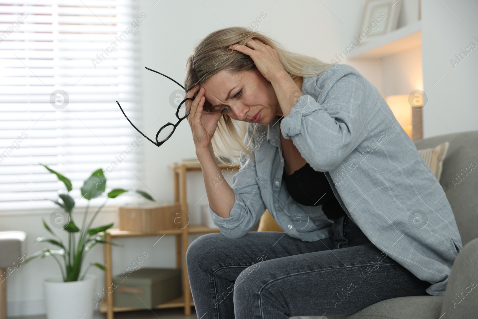 Photo of Menopause. Woman suffering from headache on sofa at home