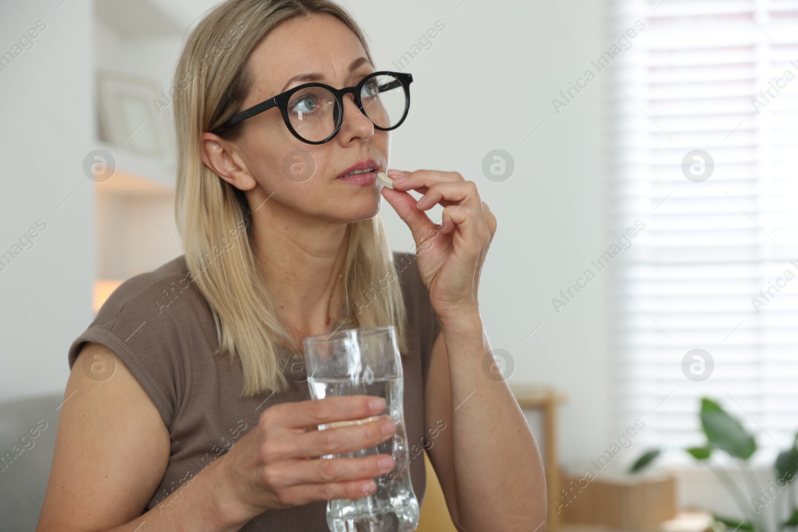 Photo of Menopause, hormone replacement therapy. Woman with glass of water taking pill at home, space for text