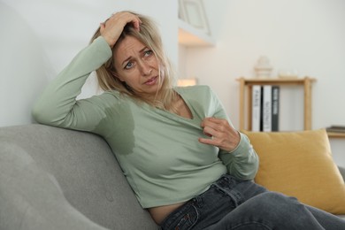 Photo of Menopause. Woman suffering from hot flash on sofa at home