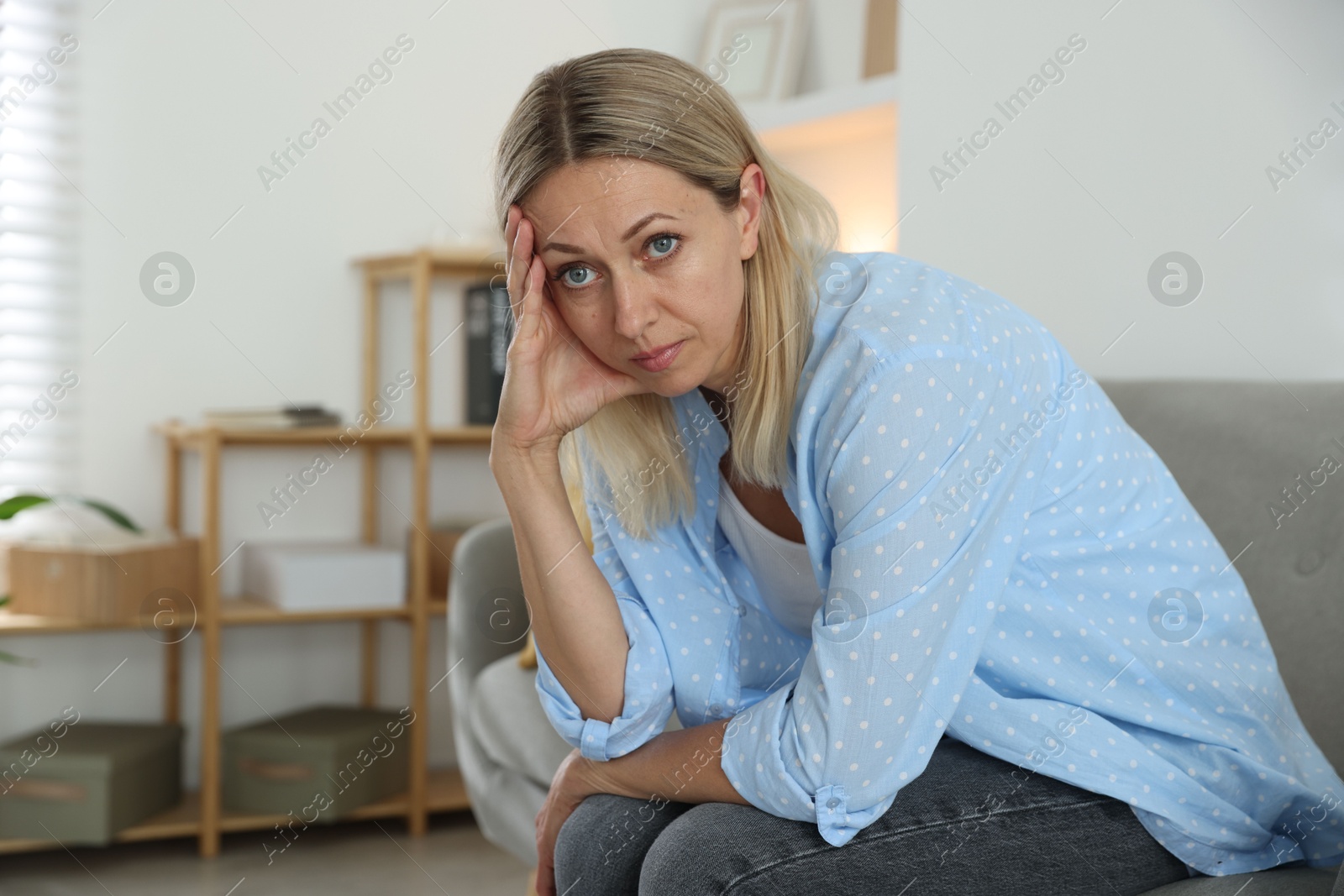 Photo of Menopause. Woman suffering from headache on sofa at home, space for text