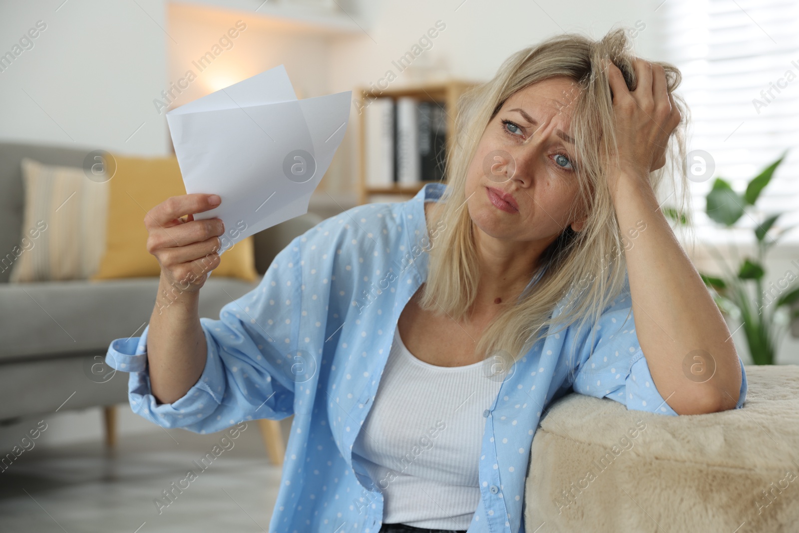 Photo of Menopause. Woman waving paper sheet to cool herself during hot flash at home