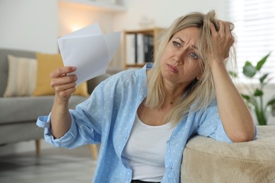 Menopause. Woman waving paper sheet to cool herself during hot flash at home