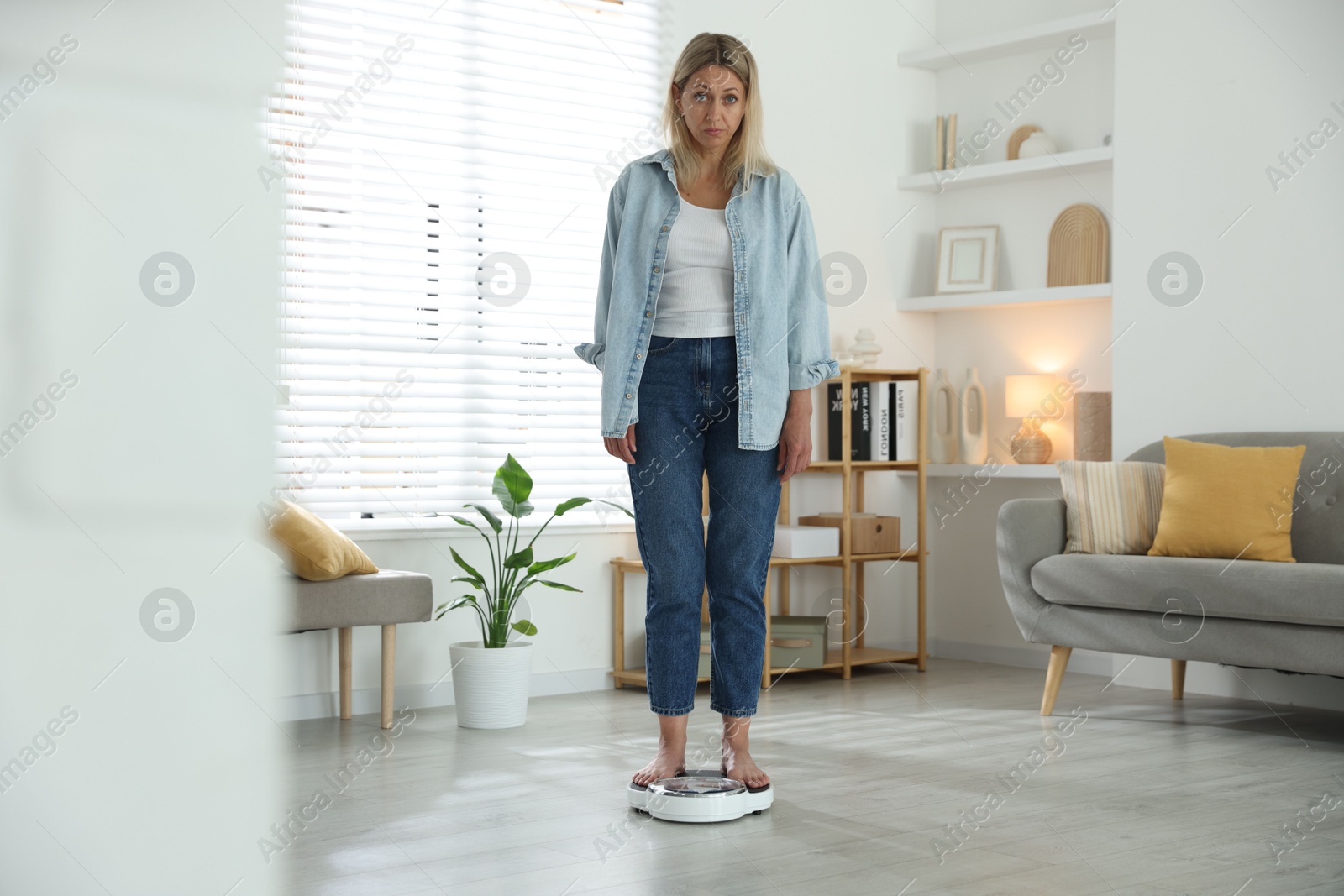 Photo of Menopause, weight gain. Concerned woman standing on floor scales at home