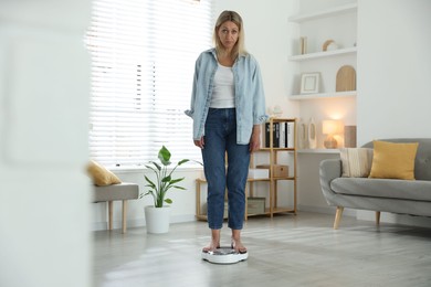 Photo of Menopause, weight gain. Concerned woman standing on floor scales at home