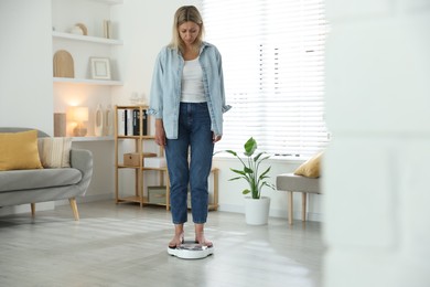 Menopause, weight gain. Concerned woman standing on floor scales at home