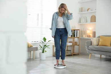 Photo of Menopause, weight gain. Concerned woman standing on floor scales at home