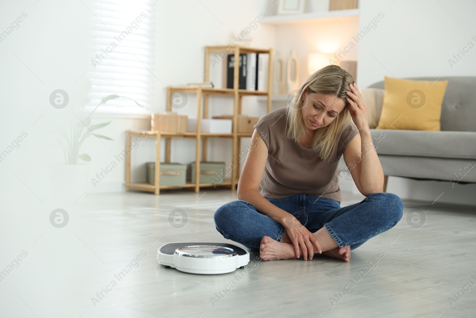 Photo of Menopause, weight gain. Concerned woman sitting near floor scales at home