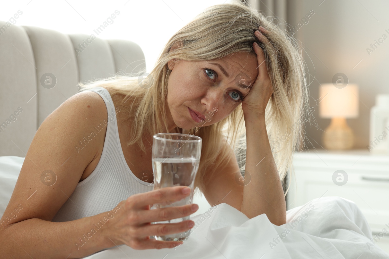 Photo of Menopause. Woman with glass of water suffering from headache in bed at home