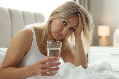 Menopause. Woman with glass of water suffering from headache in bed at home