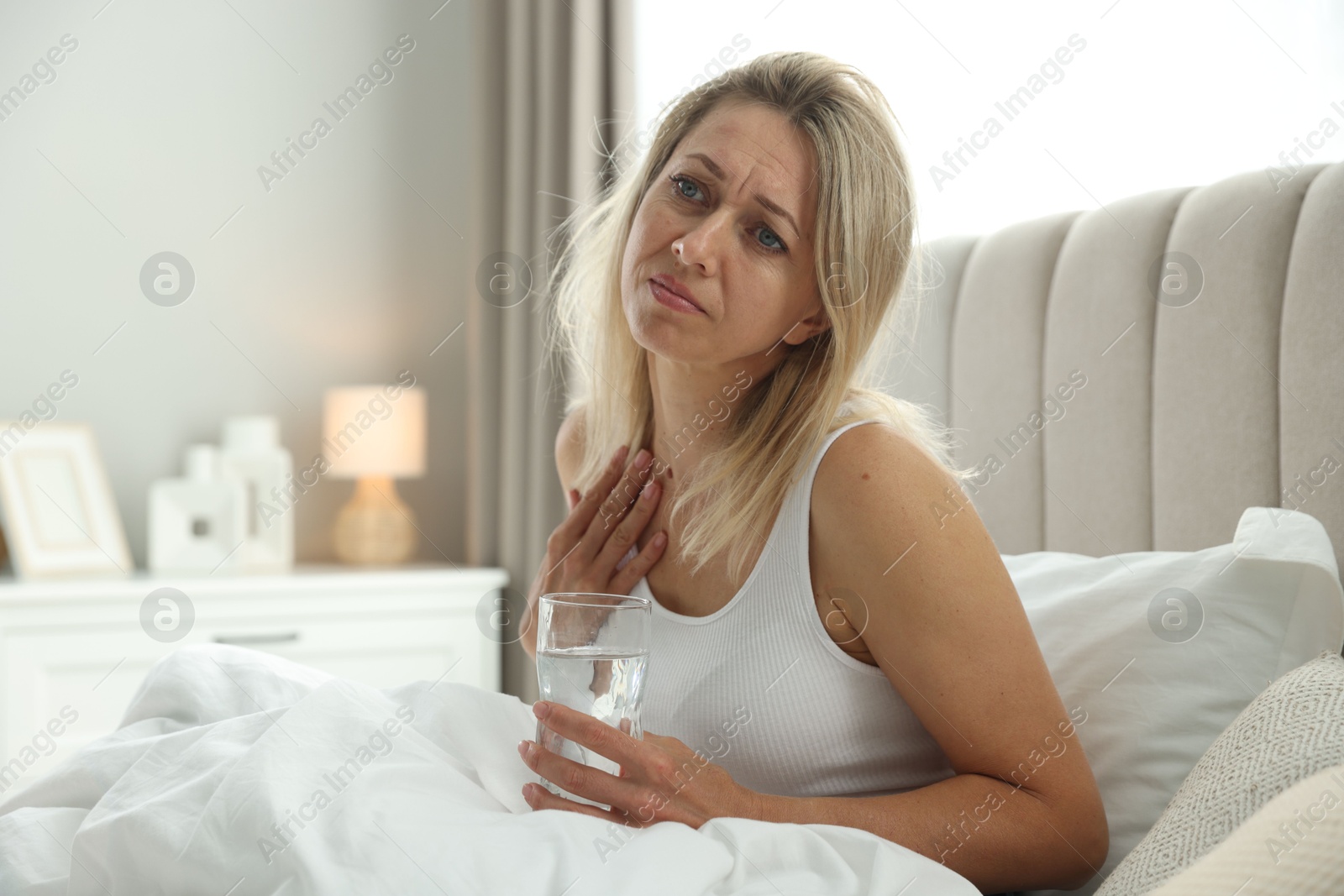 Photo of Menopause. Woman with glass of water suffering from hot flash in bed at home