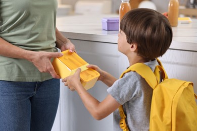 Mother giving lunch box to her son in kitchen, closeup