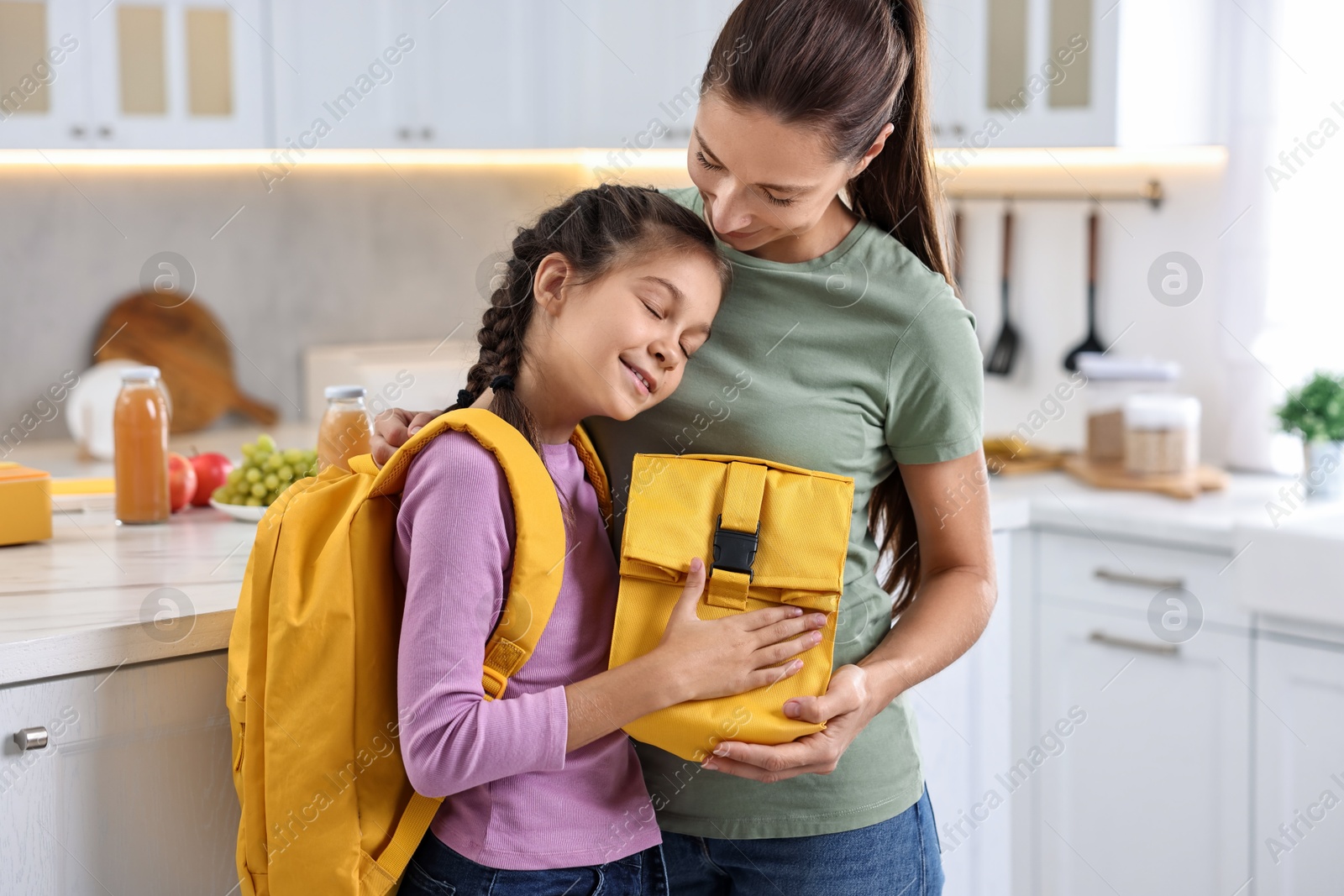 Photo of Smiling mother and her daughter with lunch bag in kitchen. Preparing for school