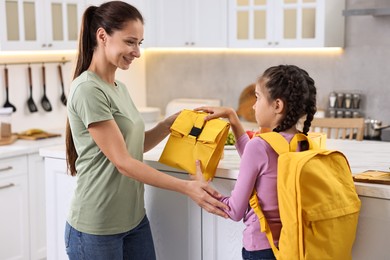 Photo of Smiling mother giving lunch bag to her daughter in kitchen. Preparing for school