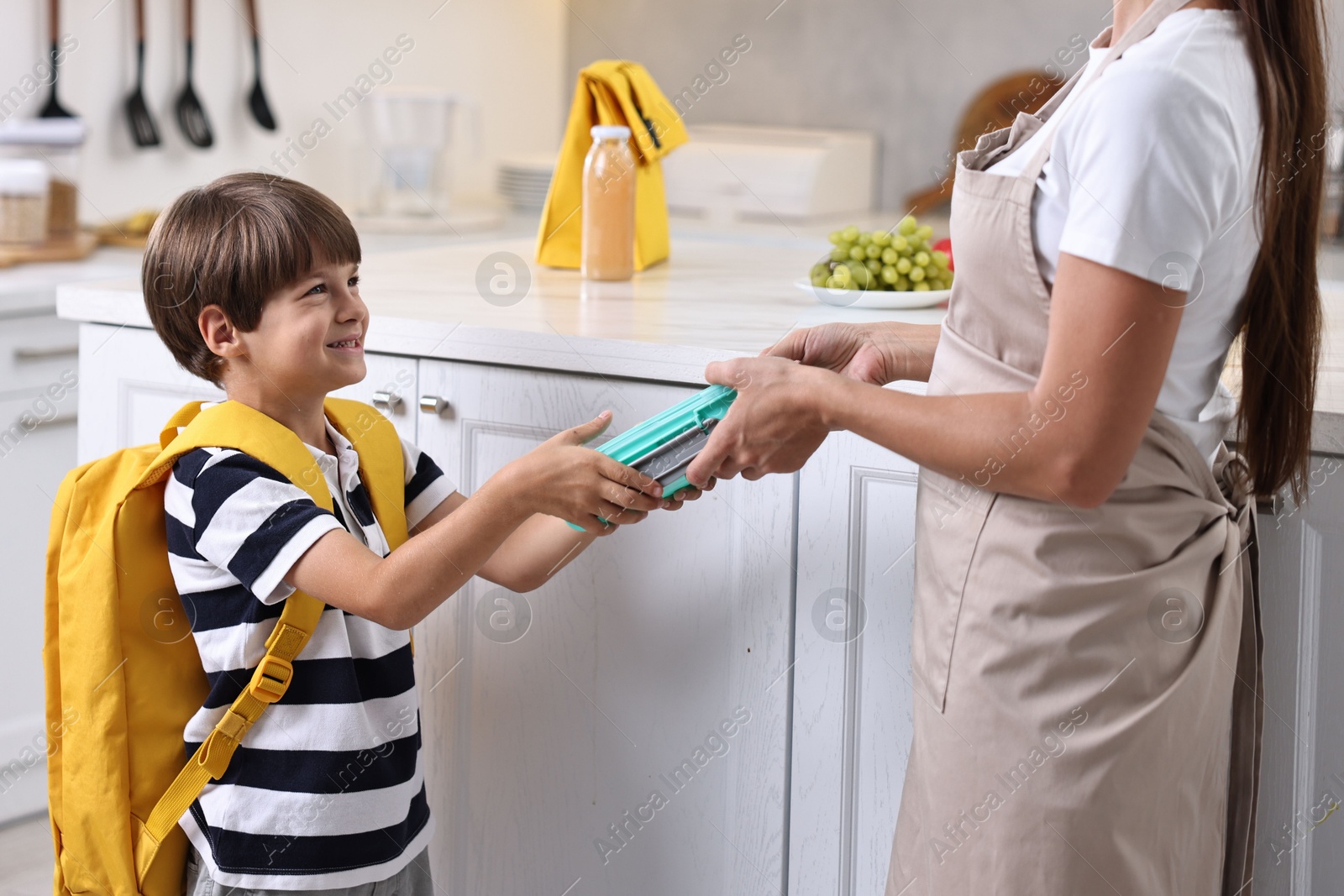 Photo of Mother giving lunch box to her son in kitchen, closeup