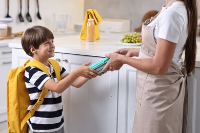 Mother giving lunch box to her son in kitchen, closeup