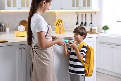 Photo of Mother giving lunch box to her son in kitchen. Preparing for school