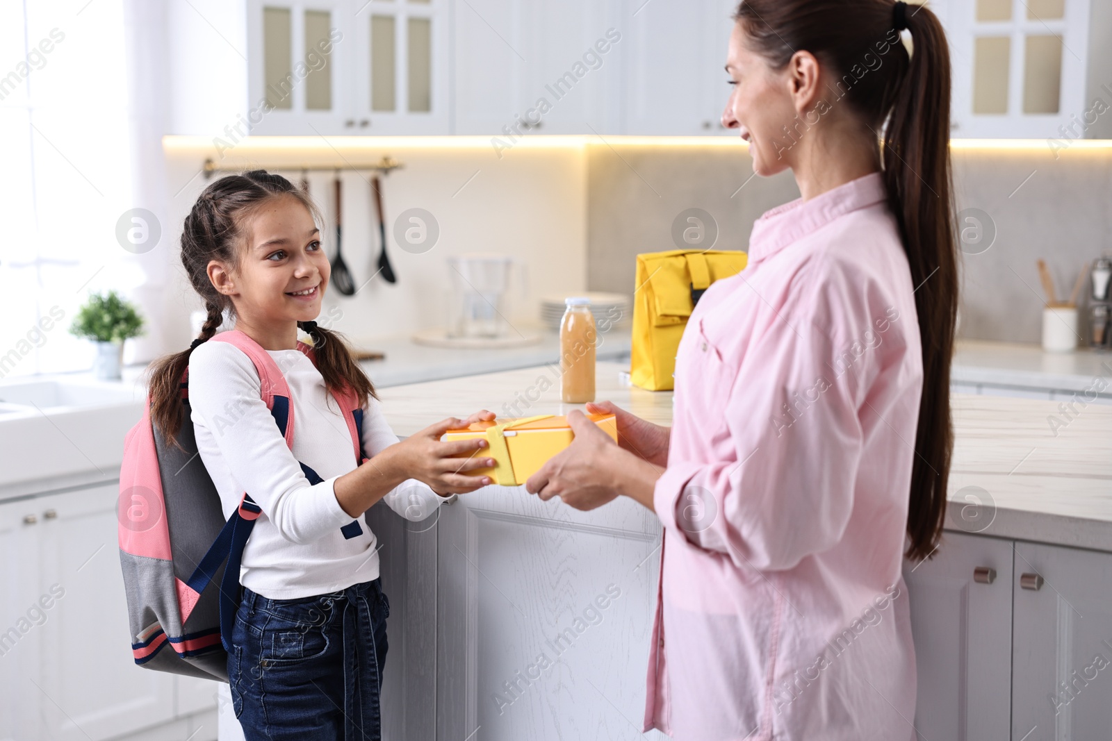 Photo of Smiling mother giving lunch box to her daughter in kitchen. Preparing for school