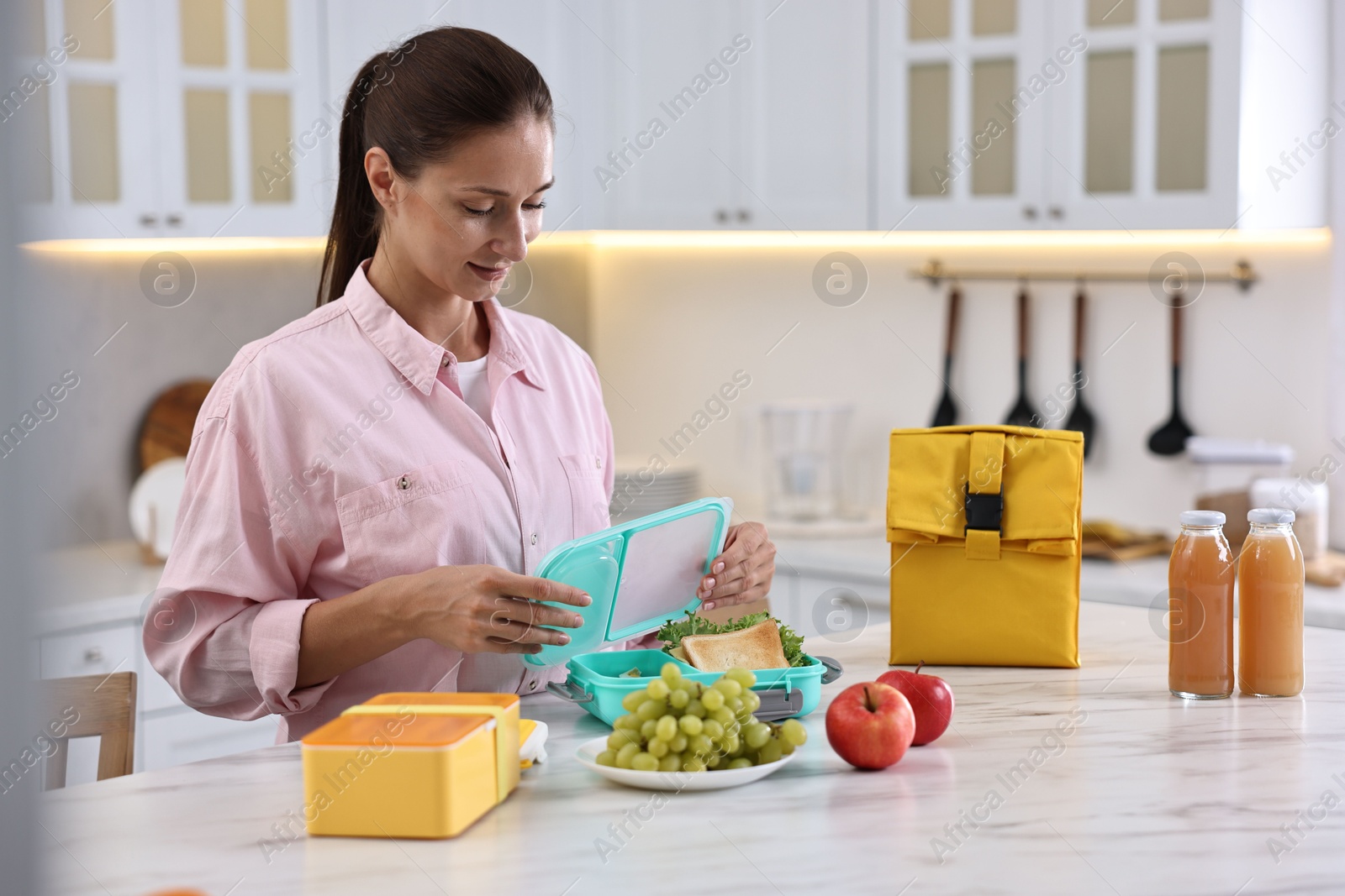 Photo of Woman packing school lunch box with healthy food at white marble table in kitchen