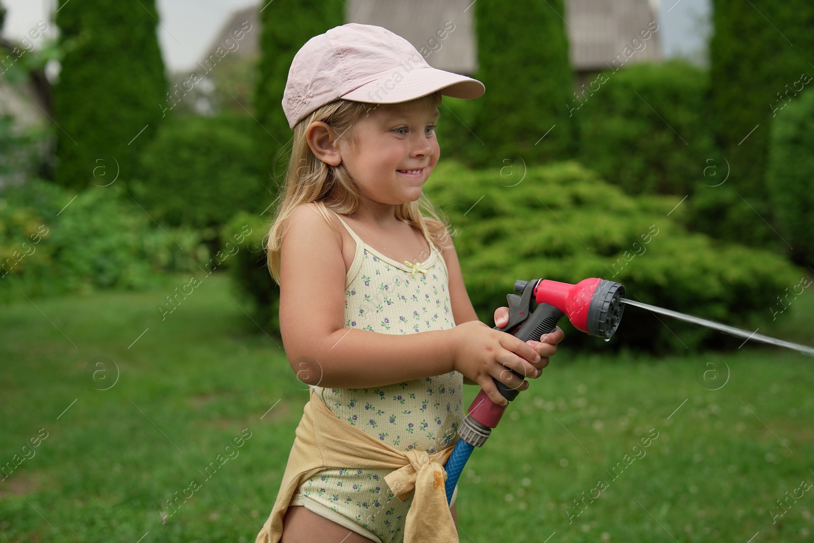 Photo of Little girl watering lawn with hose in backyard