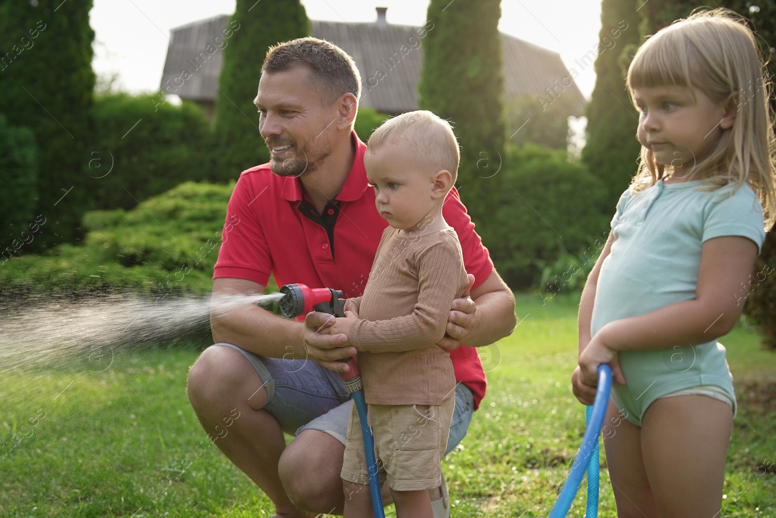 Photo of Little boy watering lawn with hose while his father and sister watching in backyard