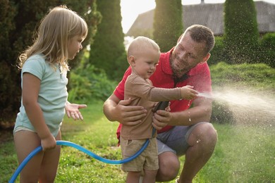 Photo of Little boy watering lawn with hose while his father and sister watching in backyard