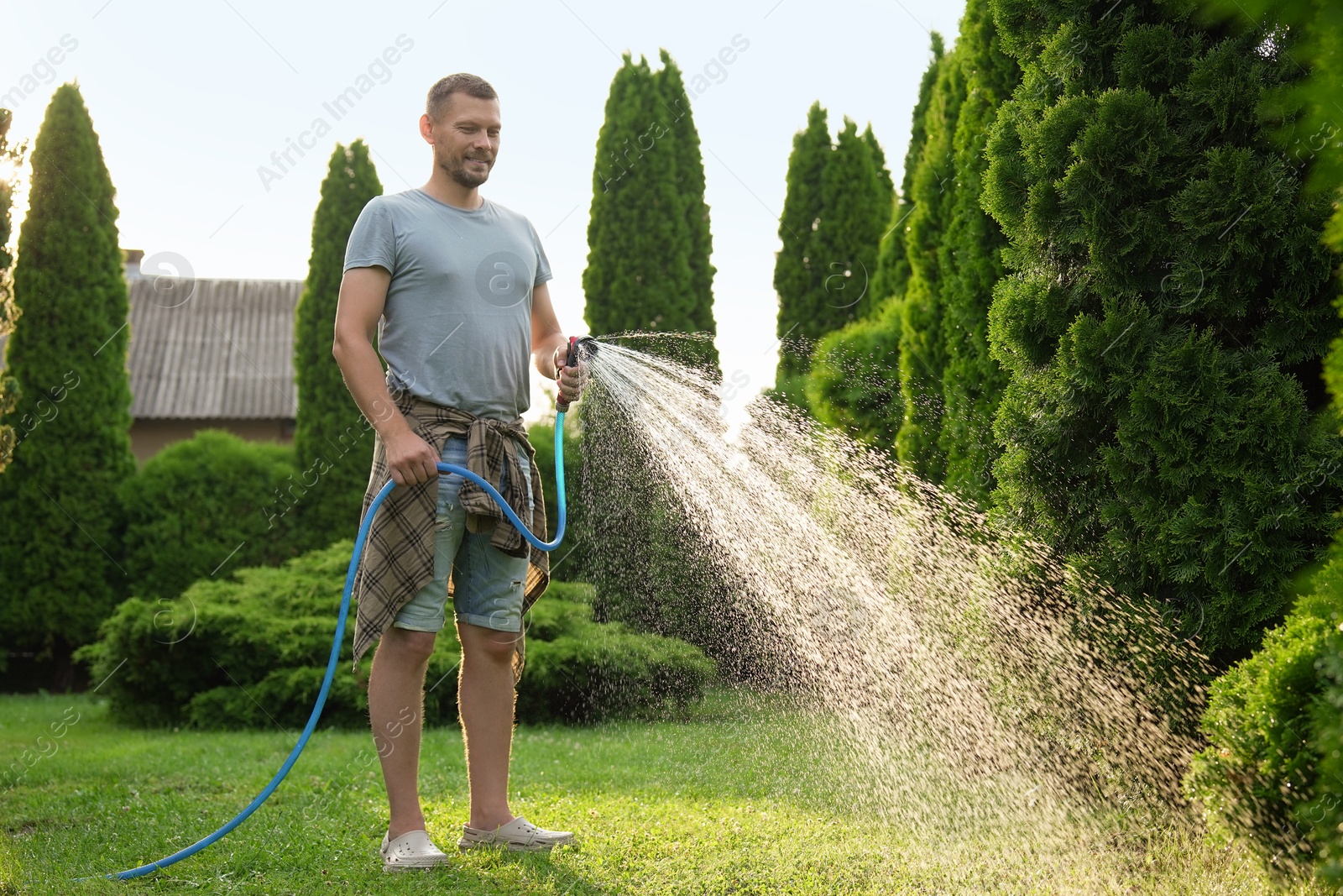 Photo of Man watering lawn with hose in backyard