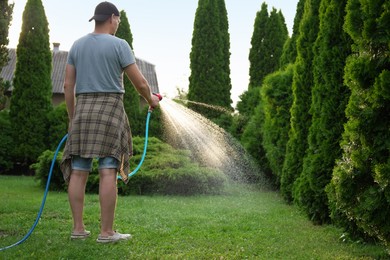 Man watering lawn with hose in backyard, back view