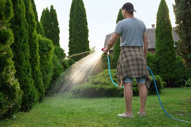 Man watering lawn with hose in backyard, back view