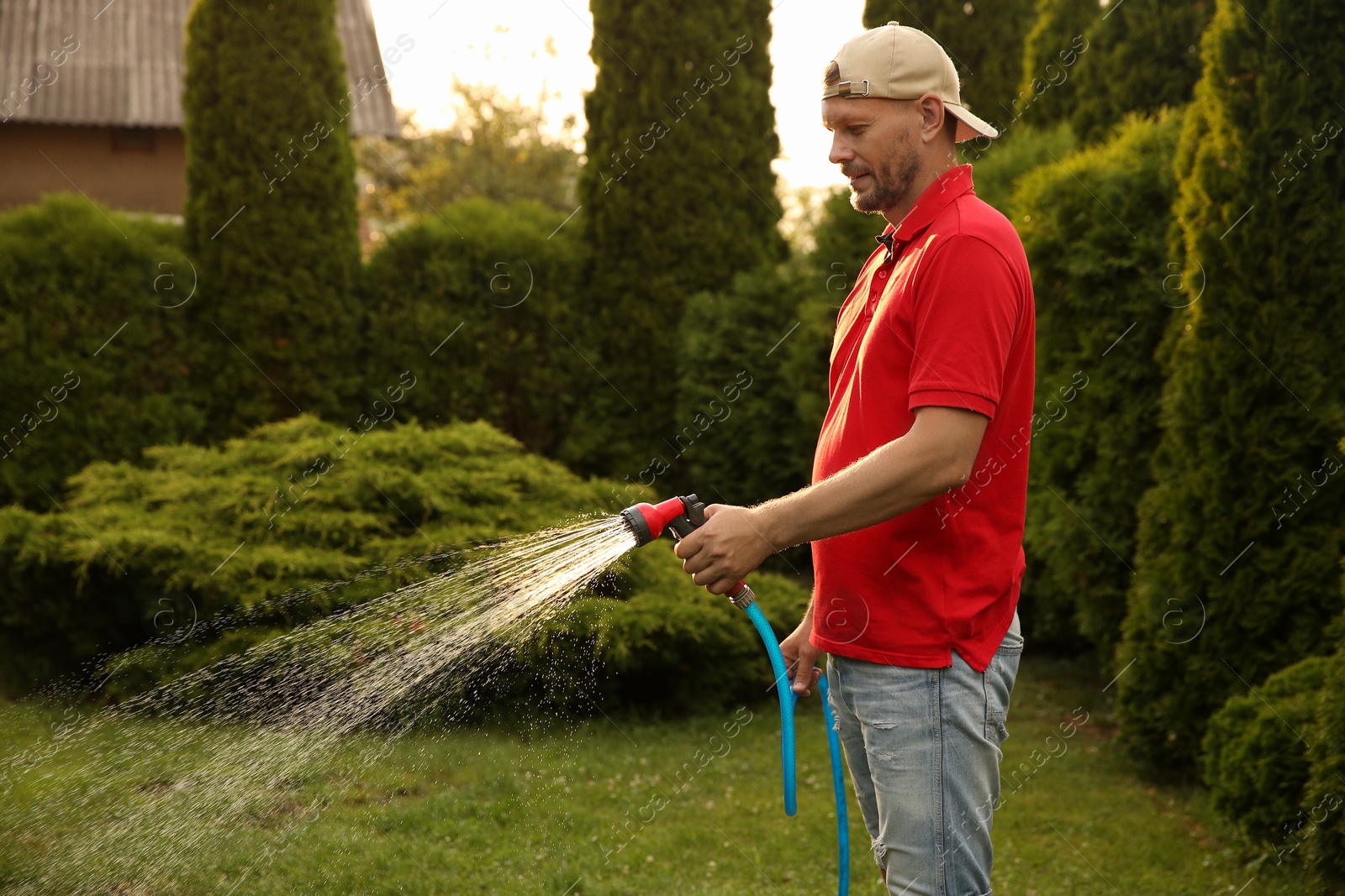 Photo of Man watering lawn with hose in backyard