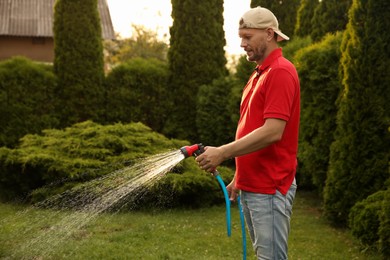 Photo of Man watering lawn with hose in backyard