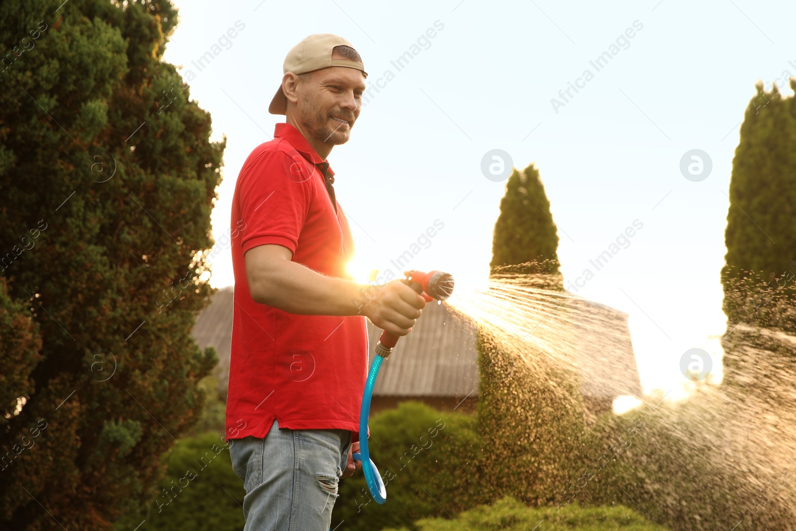 Photo of Man watering lawn with hose in backyard on sunny day