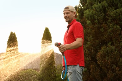 Photo of Man watering lawn with hose in backyard on sunny day